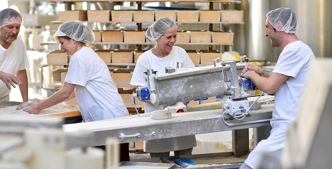 fröhliche Arbeiter bei der Herstellung von Backwaren und Broten in einer Großbäckerei // cheerful workers in the industrial production of bread in a bakery