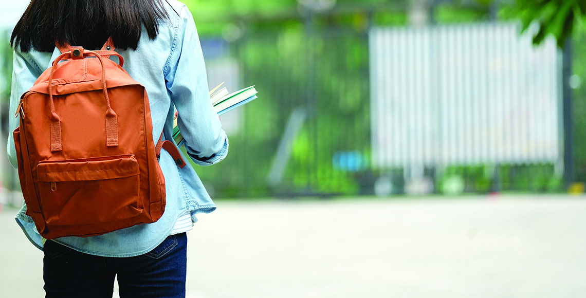 Back of student girl holding books and carry school bag while walking in school campus background, copy space banner, education, back to school concept
