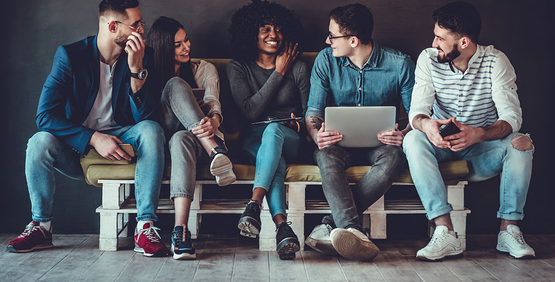 Happy diverse friends group sharing social media app news sitting holding phones, smiling multiracial young people students showing funny videos on laptop